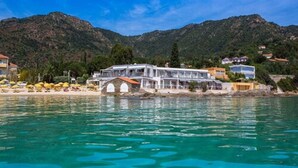 A coastal hotel with a large building, a bridge, and a beach with umbrellas. - Roc Hotel (Le Lavandou)