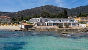 A coastal hotel with multiple buildings, a beach, and a mountainous backdrop. - Roc Hotel (Le Lavandou)