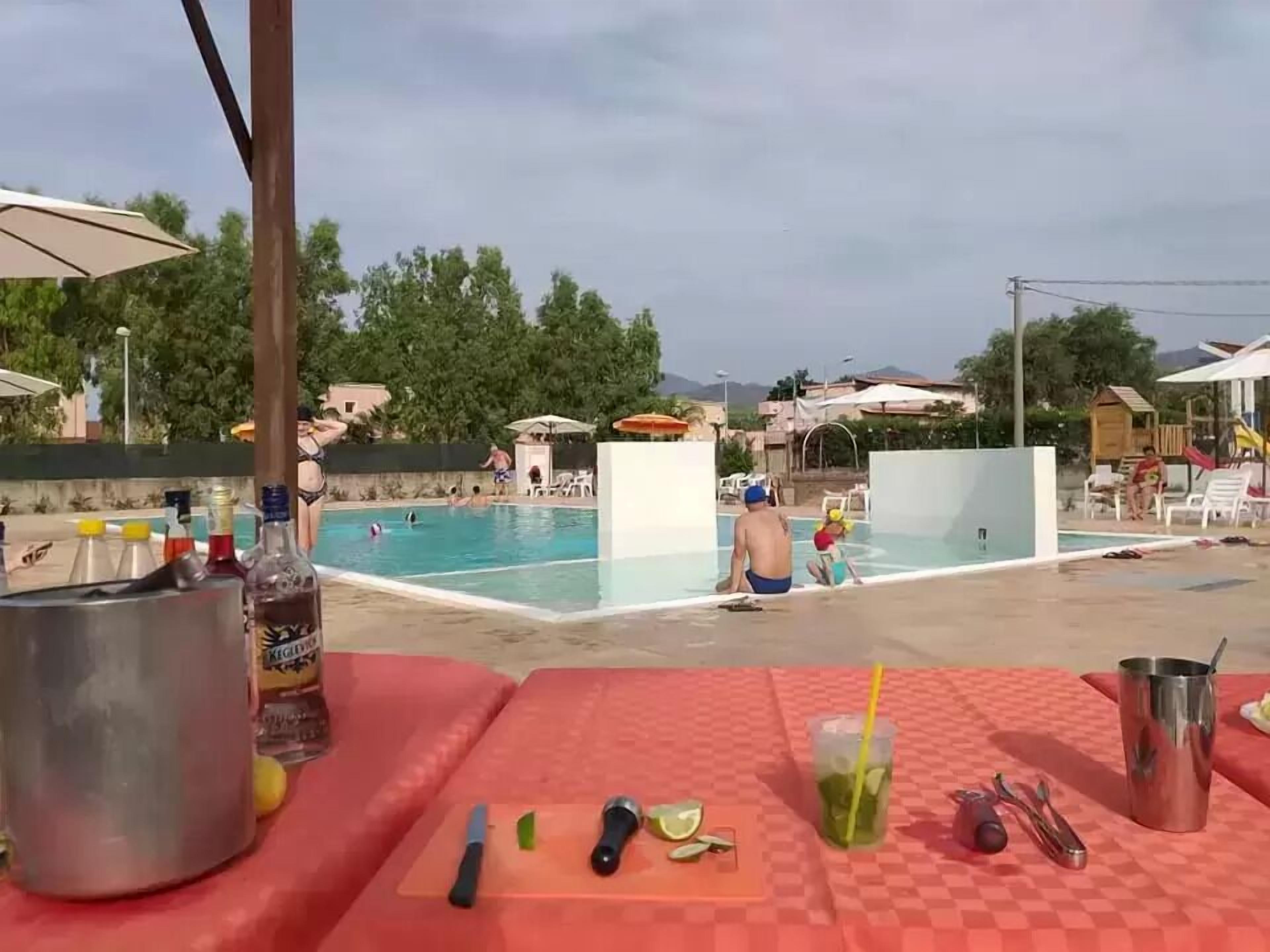 A poolside area with lounge chairs, a table with drinks and snacks, and a view of the pool and guests.