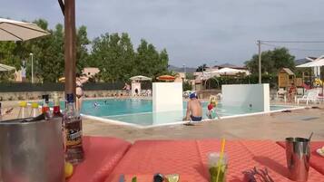 A poolside area with lounge chairs, a table with drinks and snacks, and a view of the pool and guests.