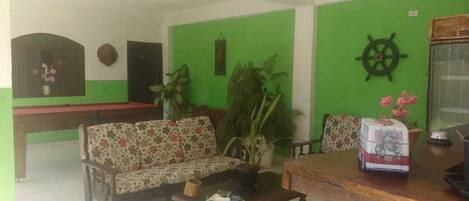 Un salon comprenant un canapé, une table basse, une petite table sur laquelle est posé un modèle de vélo, et un mur vert orné d’une décoration représentant un gouvernail de bateau.
