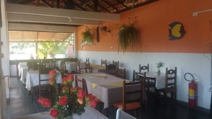 Restaurante com mesas postas, extintor de incêndio e plantas penduradas.