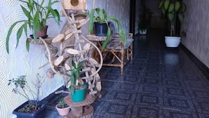 Um corredor com uma escultura de pássaro em madeira, plantas em vasos e chão de azulejos.