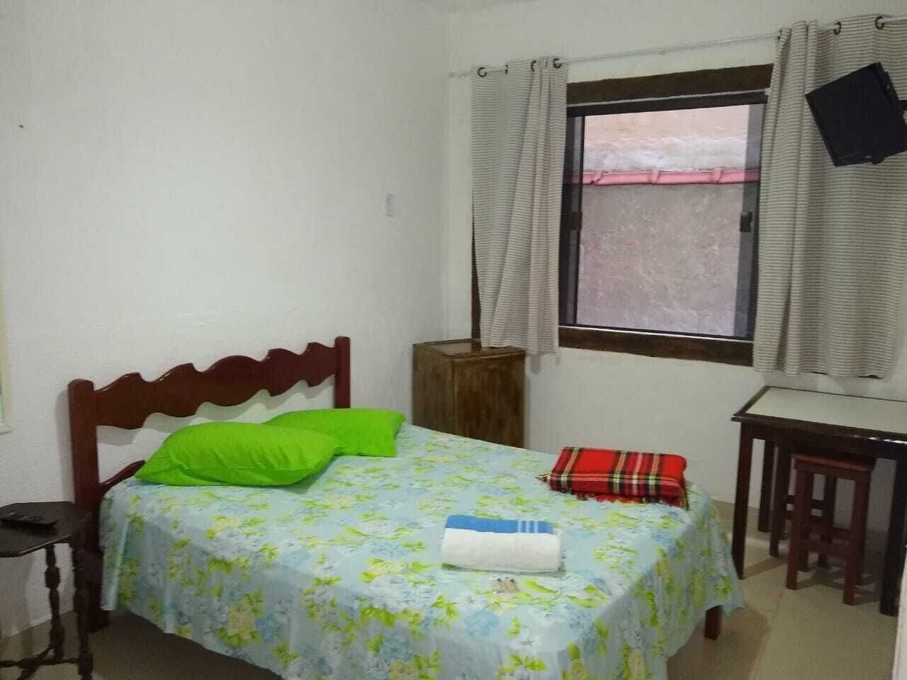 Um quarto pequeno e simples com uma cama, uma escrivaninha e uma janela com cortinas.