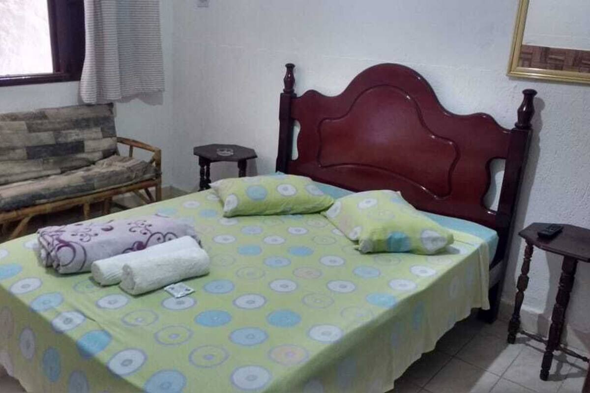 Une pièce comprenant un lit, une tête de lit en bois, une petite table et une chaise.