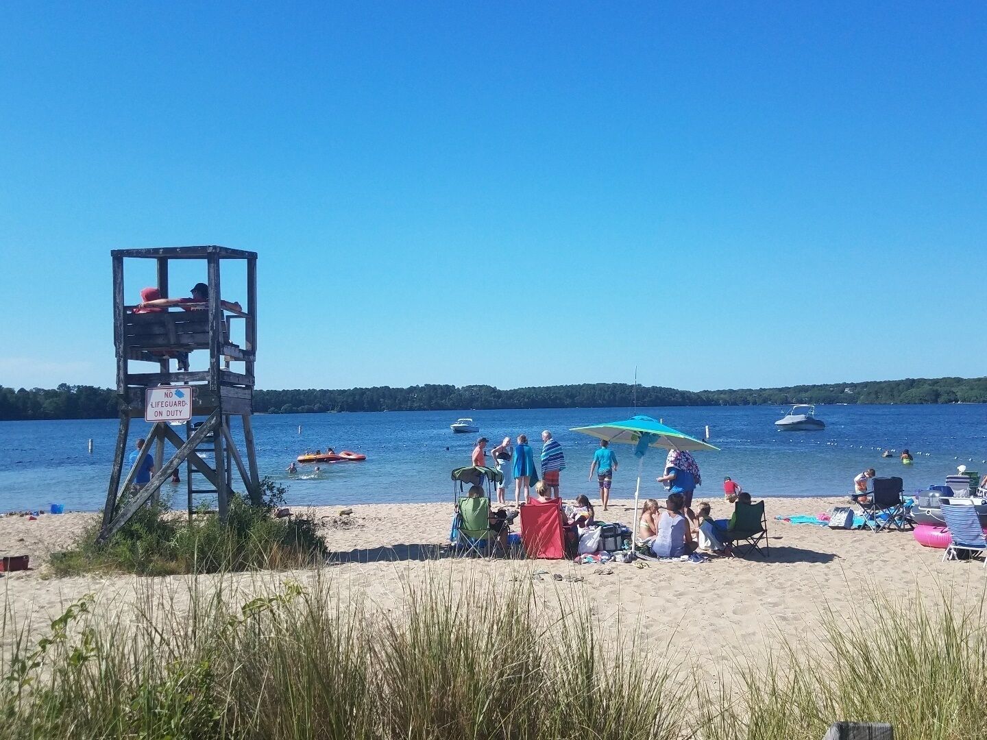 A beach with a lifeguard tower, people relaxing, and boats on the water.