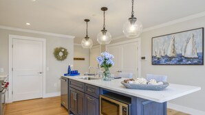 Une cuisine moderne dotée d’un îlot central, de luminaires suspendus et d’un tableau sur le thème de la marine.