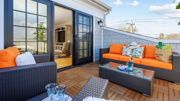 An outdoor patio area with wicker furniture, a glass coffee table, and a view of the interior through glass doors. - TJs Tide: Prime Location Condo w/ Outdoor Deck (Harwich Port)