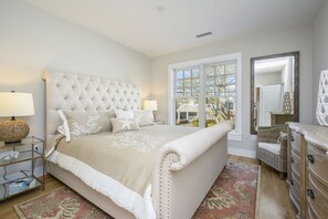 A bedroom with a large bed, a nightstand, a dresser, and a large window with a view of the outside.