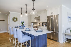 A modern kitchen with a central island, stainless steel appliances, and blue-striped bar stools.