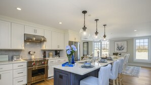 A modern kitchen with white cabinetry, stainless steel appliances, and a central island with bar seating. - TJs Tide: Prime Location Condo w/ Outdoor Deck (Harwich Port)
