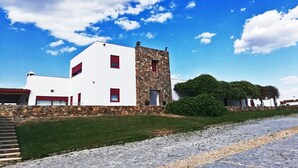 A modern building with a white facade and red accents, a stone tower, and a paved driveway.
