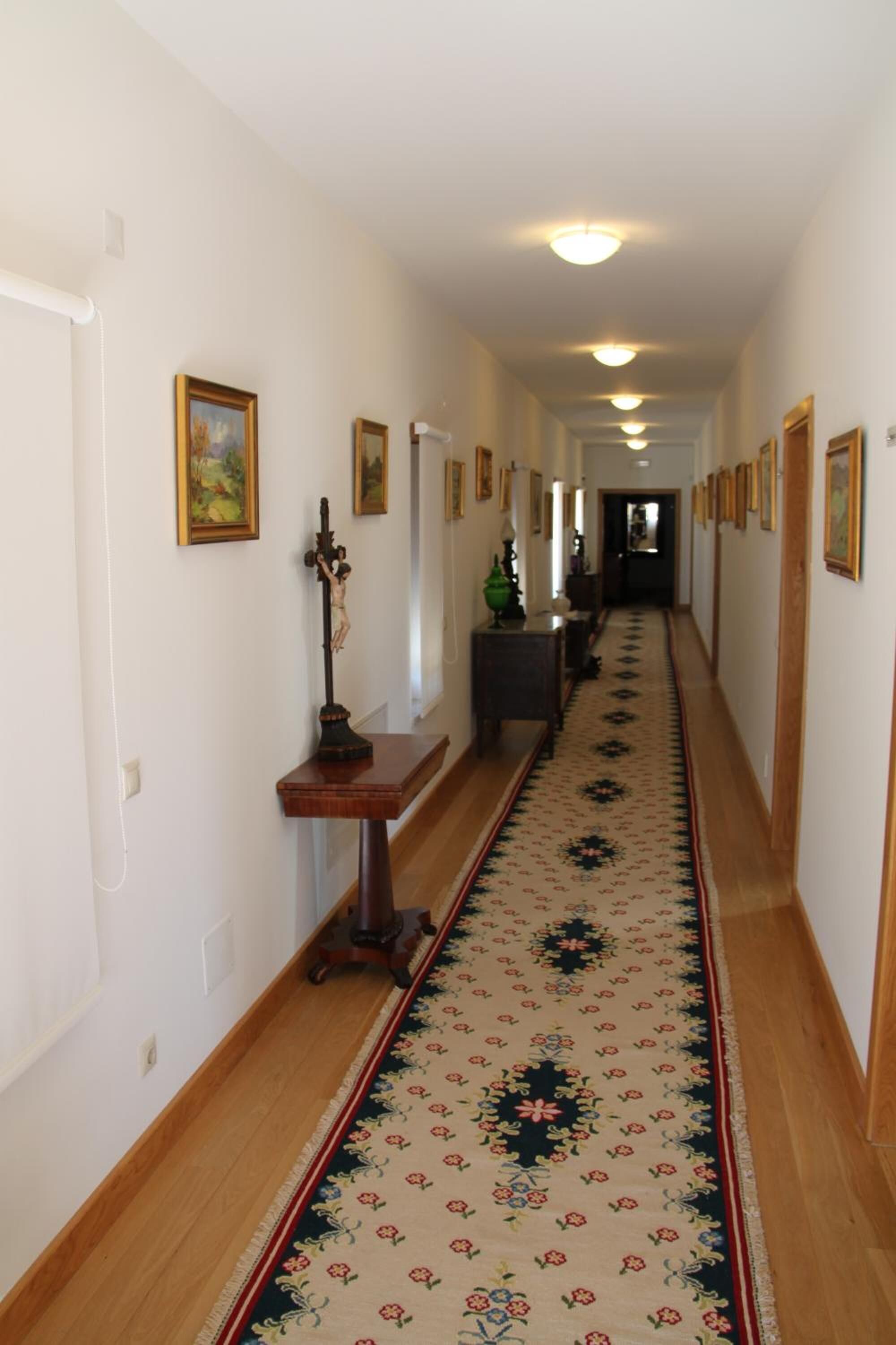 A long hallway with wooden floors, a patterned carpet, and framed pictures on the walls.