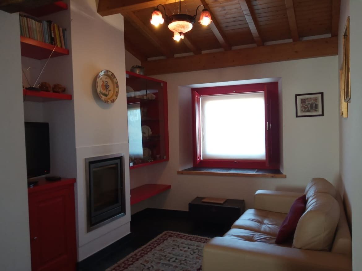 Una sala de estar con chimenea, sofá, ventana con detalles rojos y una estantería.