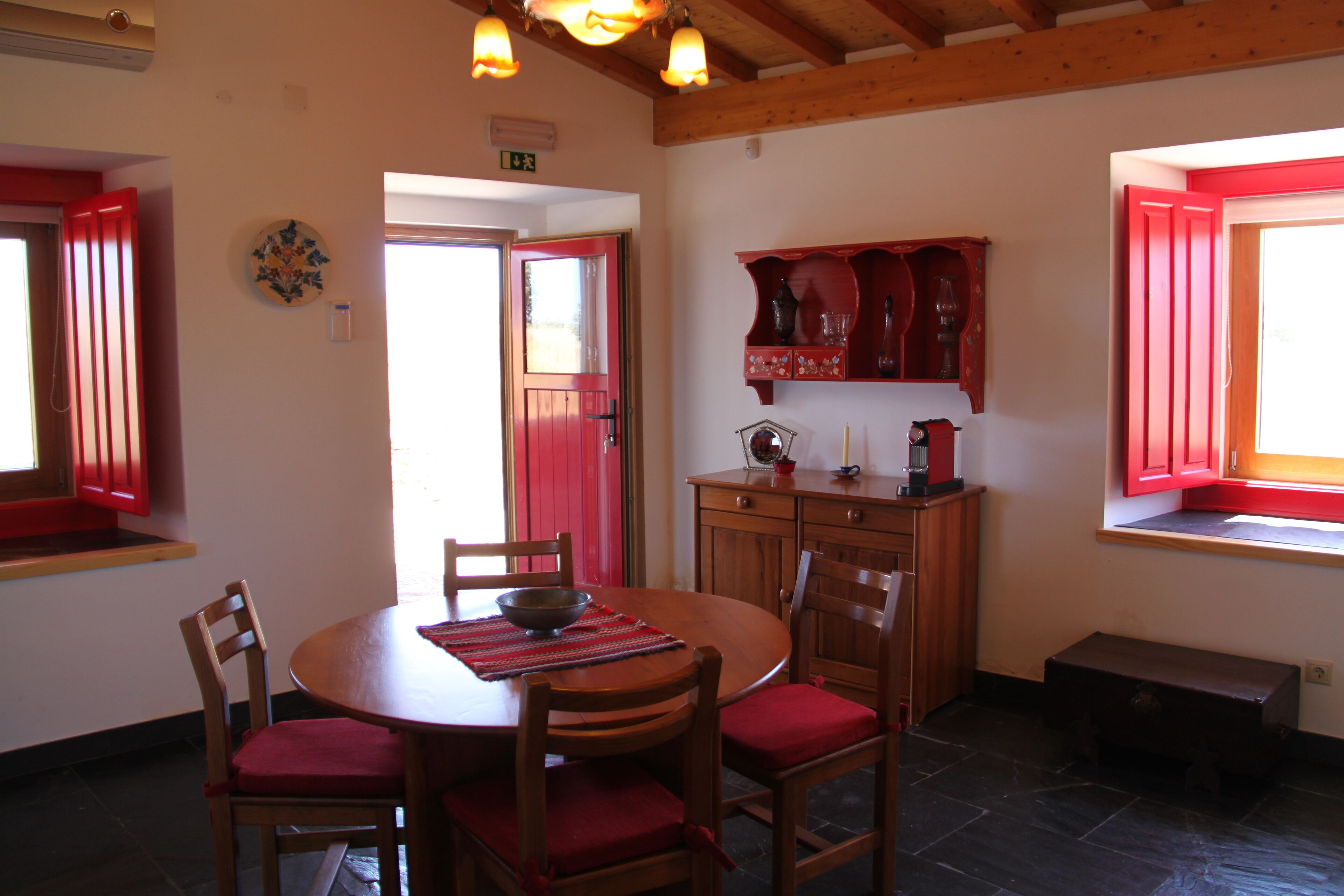 A dining area with a round wooden table, red cushioned chairs, and a red cabinet above the counter.