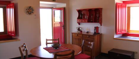 A dining area with a round wooden table, red cushioned chairs, and a red cabinet above the counter.