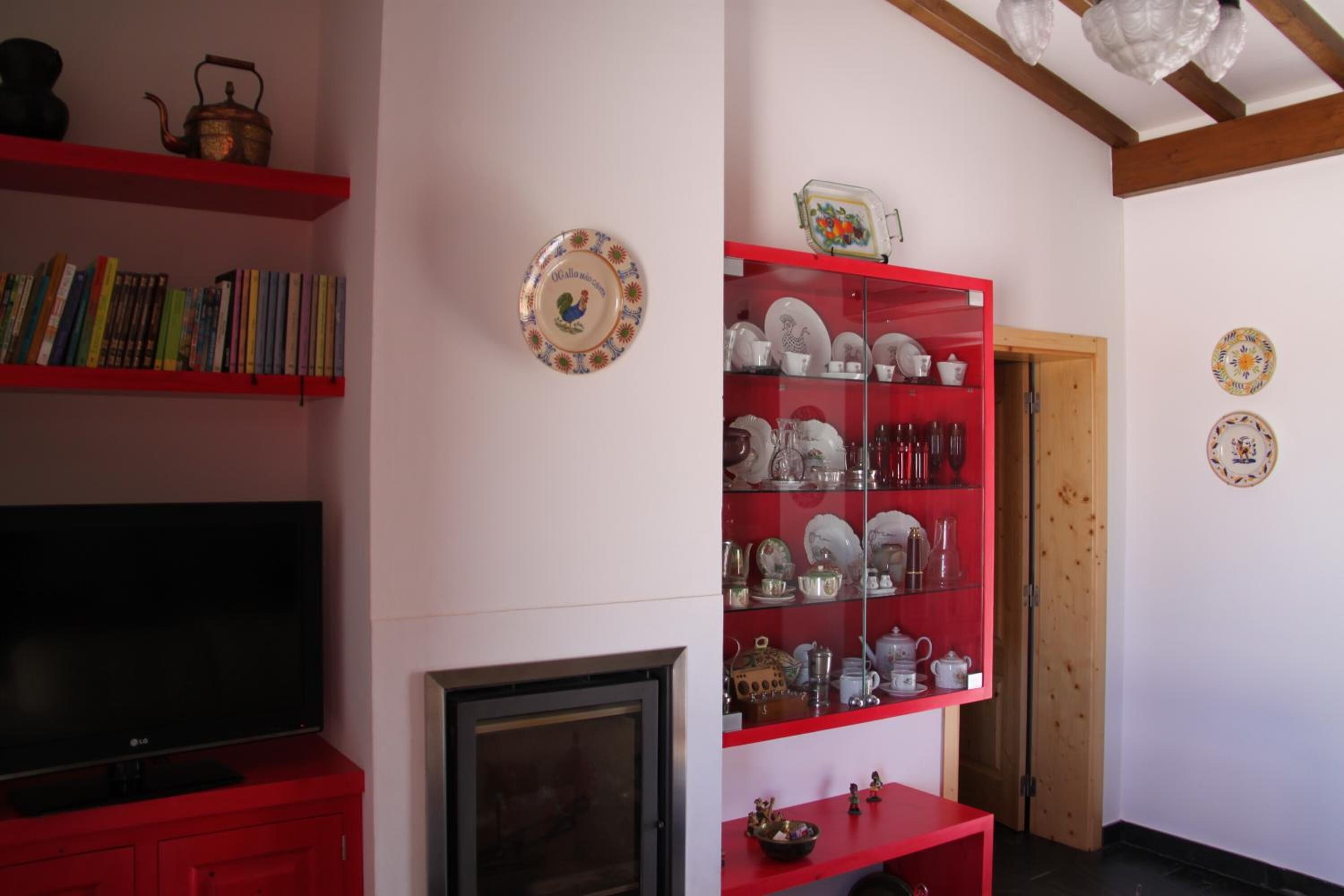 Una sala de estar con un mueble rojo para televisor, una chimenea y una estantería roja que exhibe diversos platos y teteras.