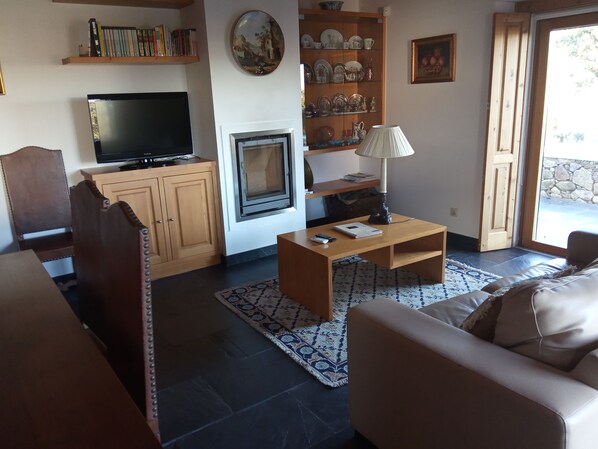 Uma sala de estar com televisão, armários de madeira, lareira, mesa de centro e sofá.