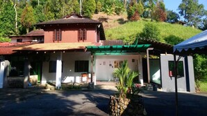 A two-story building with a red roof and a green awning, surrounded by lush greenery and hills. - Lembin Village Sdn Bhd (Sungai Lembing)