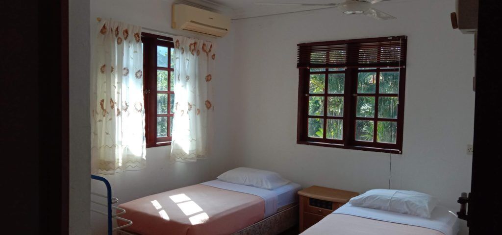 Ein Zimmer mit zwei Betten, einem Deckenventilator und einem Fenster mit Rollläden.