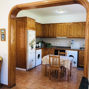 Compact kitchen with a dining area, featuring a refrigerator, washing machine, and dining table.