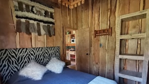A wooden interior with a bed, zebra-patterned headboard, and a door leading to a kitchen area. - Rustic cabins Pucón Pellín, rustic style, fully equipped. (Pucón)