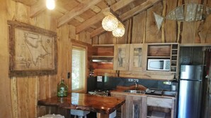 A rustic kitchen with wooden walls, a wooden bar with stools, a gas stove, a microwave, and a refrigerator. - Rustic cabins Pucón Pellín, rustic style, fully equipped. (Pucón)