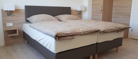 A modern bedroom with a dark headboard, two bedside tables with lamps, and a wooden wardrobe.