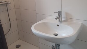Une salle de bain avec un lavabo blanc, un miroir au-dessus et un espace douche.