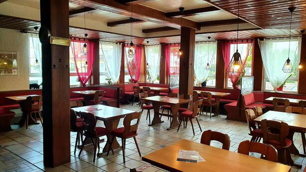 Un restaurant avec des banquettes et des tables, des poutres en bois au plafond et des rideaux aux fenêtres.