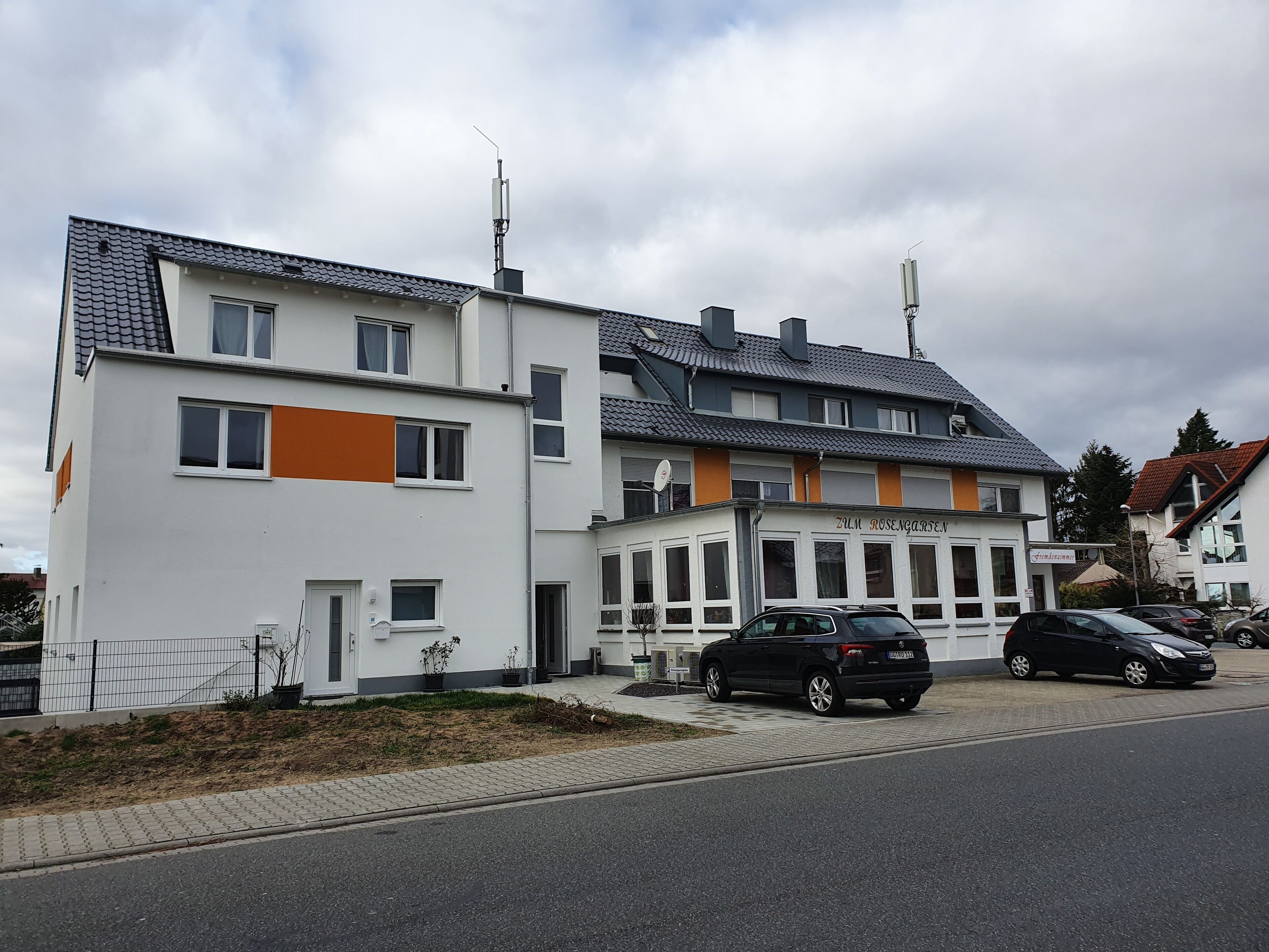 A modern two-story building with a flat roof and a sign reading "Zum Rosengarten".