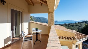 A balcony with a table and chairs, a door, and a view of a mountainous landscape.