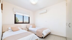 A hotel room with two beds, a window with a view, an air conditioning unit, and a tiled floor. - Private Roof Top Terrace Overlooking Pool in Pyla (Pyla)