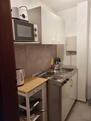 Una cocina compacta con microondas, estufa, pileta y un mueble pequeño.