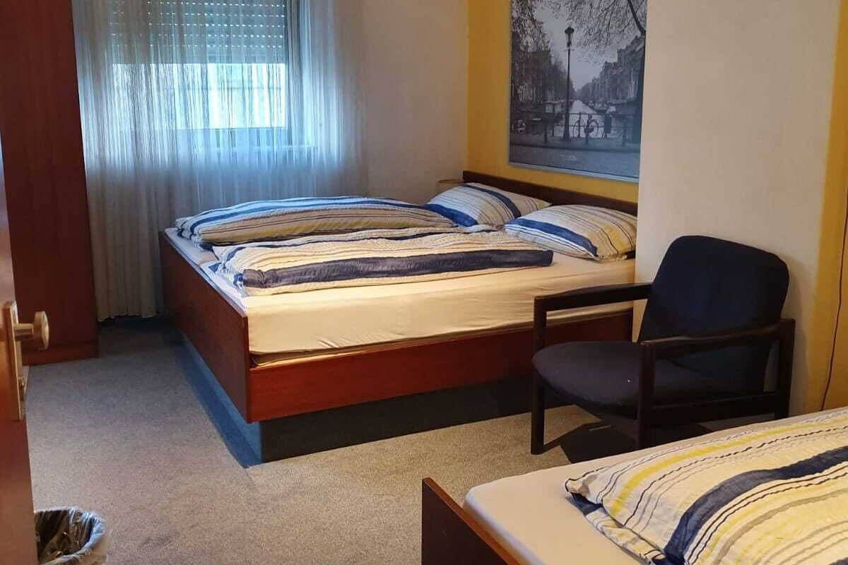 Een hotelkamer met twee bedden, een stoel, een raam met gordijnen en een schilderij aan de muur.