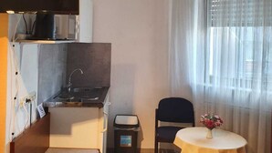 A compact room with a kitchenette, a small dining table with a chair, and a window with sheer curtains. - Hotel - Pension - Weller (Muehlheim am Main)