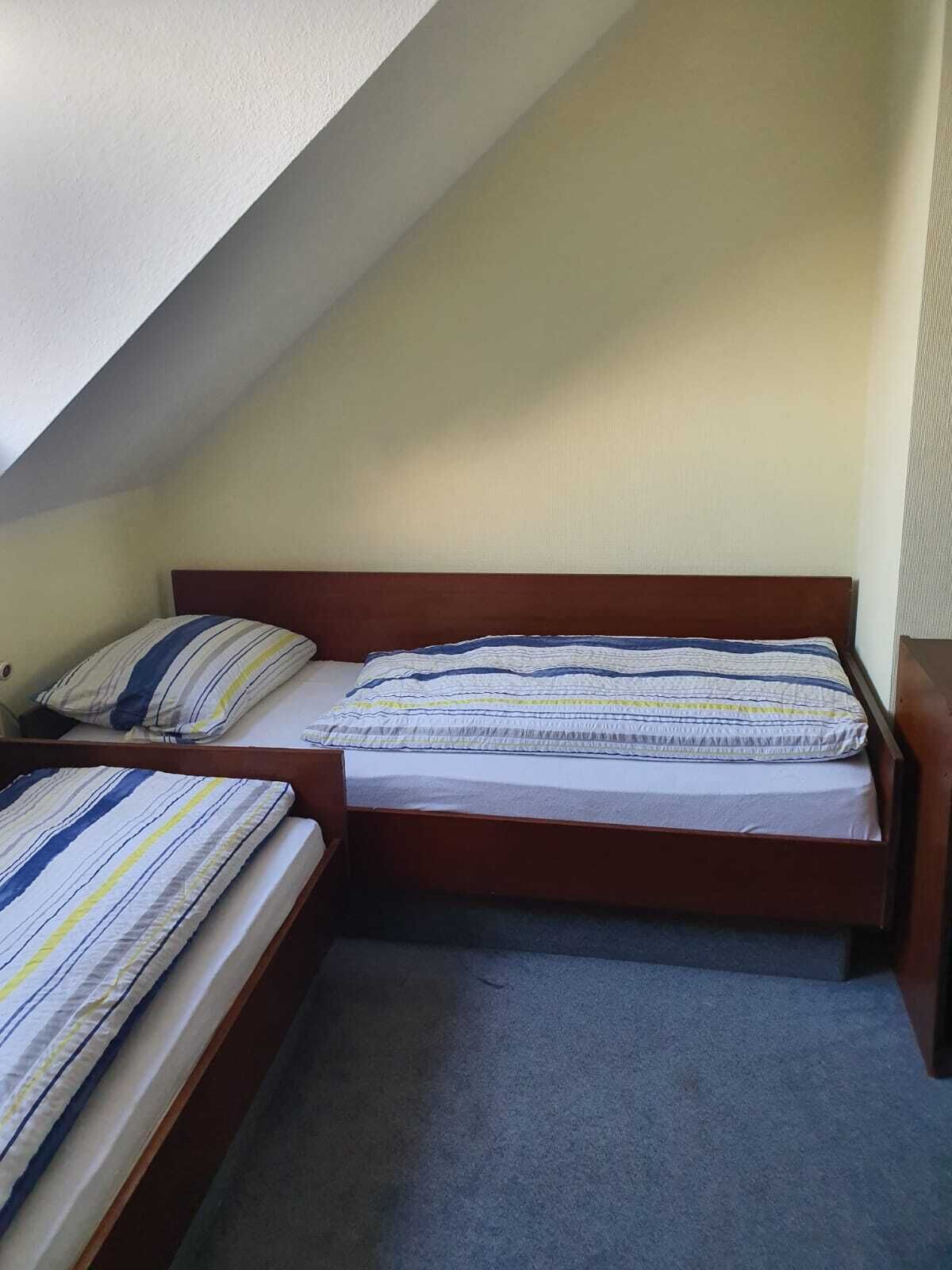 A small, single-bed room with a sloped ceiling, a wooden headboard, and a grey carpet.