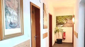 A hallway with framed artwork on the walls, wooden doors, and a potted plant. - Hotel - Pension - Weller (Muehlheim am Main)
