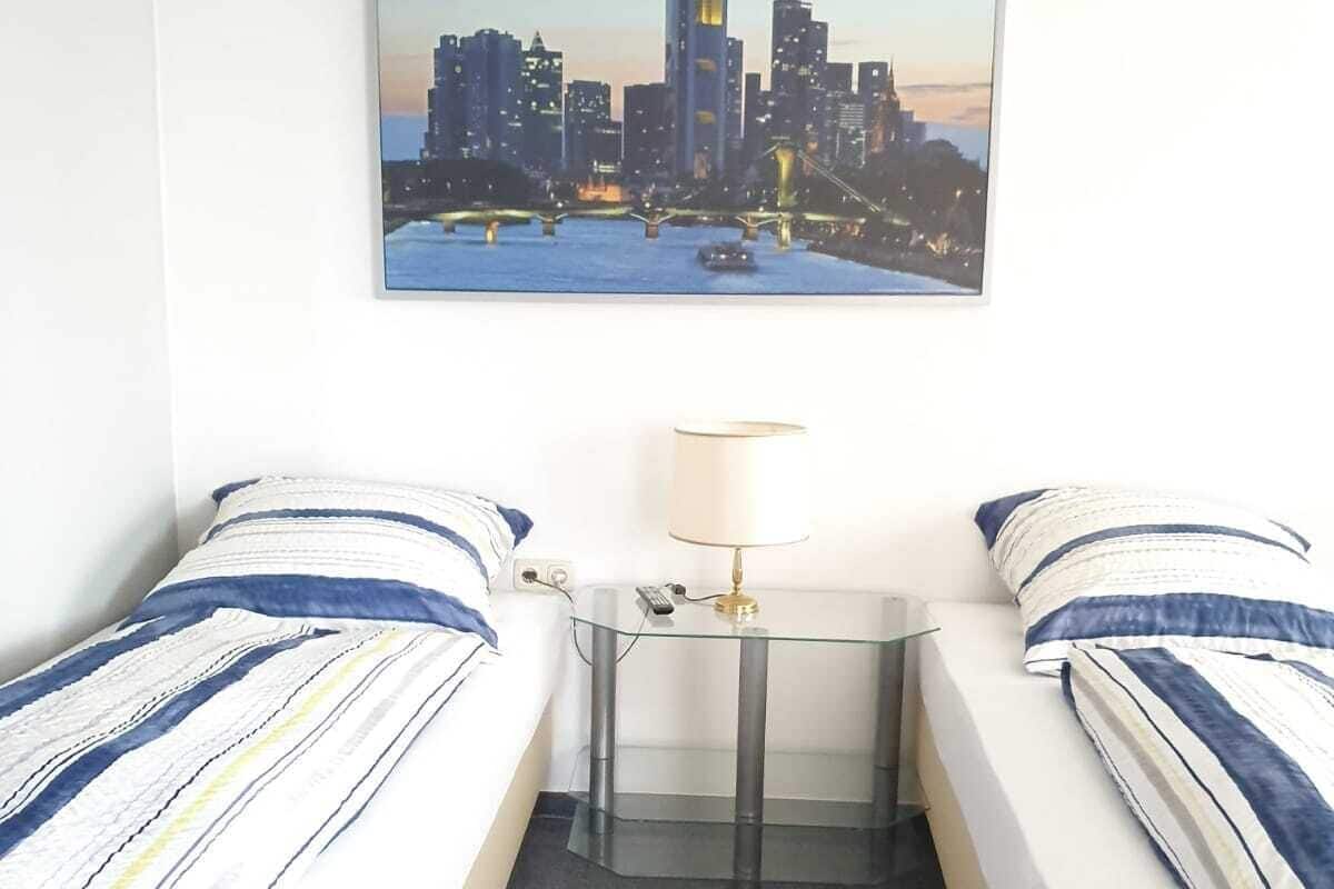 Een hotelkamer met twee bedden, een klein tafeltje met een lamp, en een stadsgezichtschilderij aan de muur.