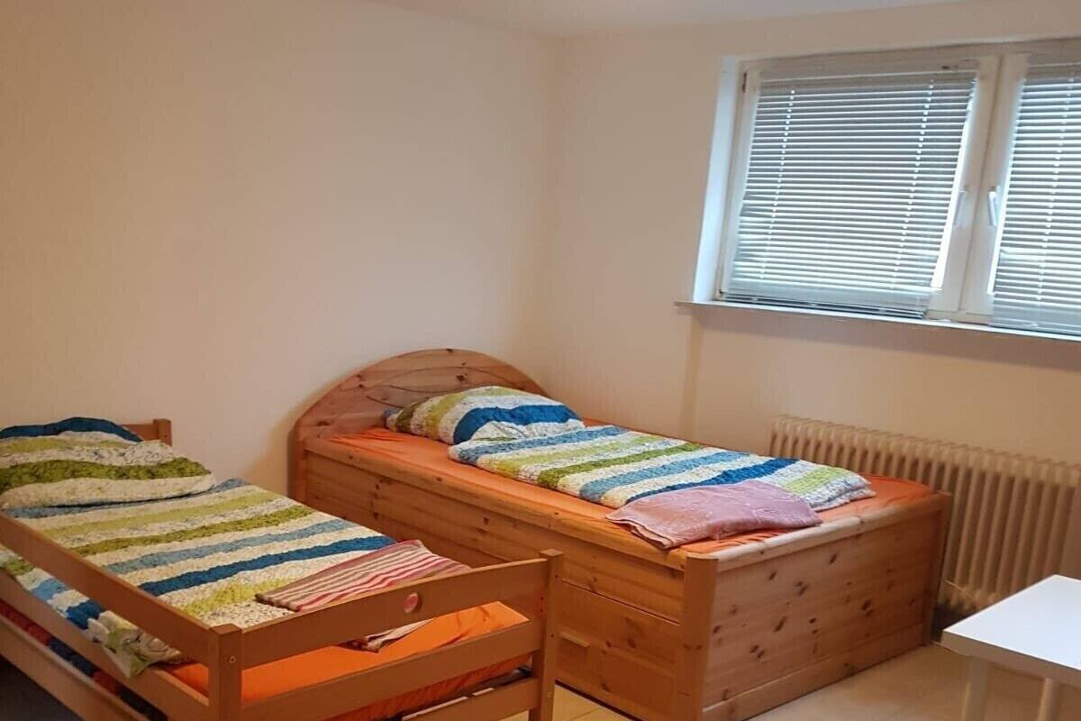 A bedroom with two wooden beds, a white table, and a window with blinds.