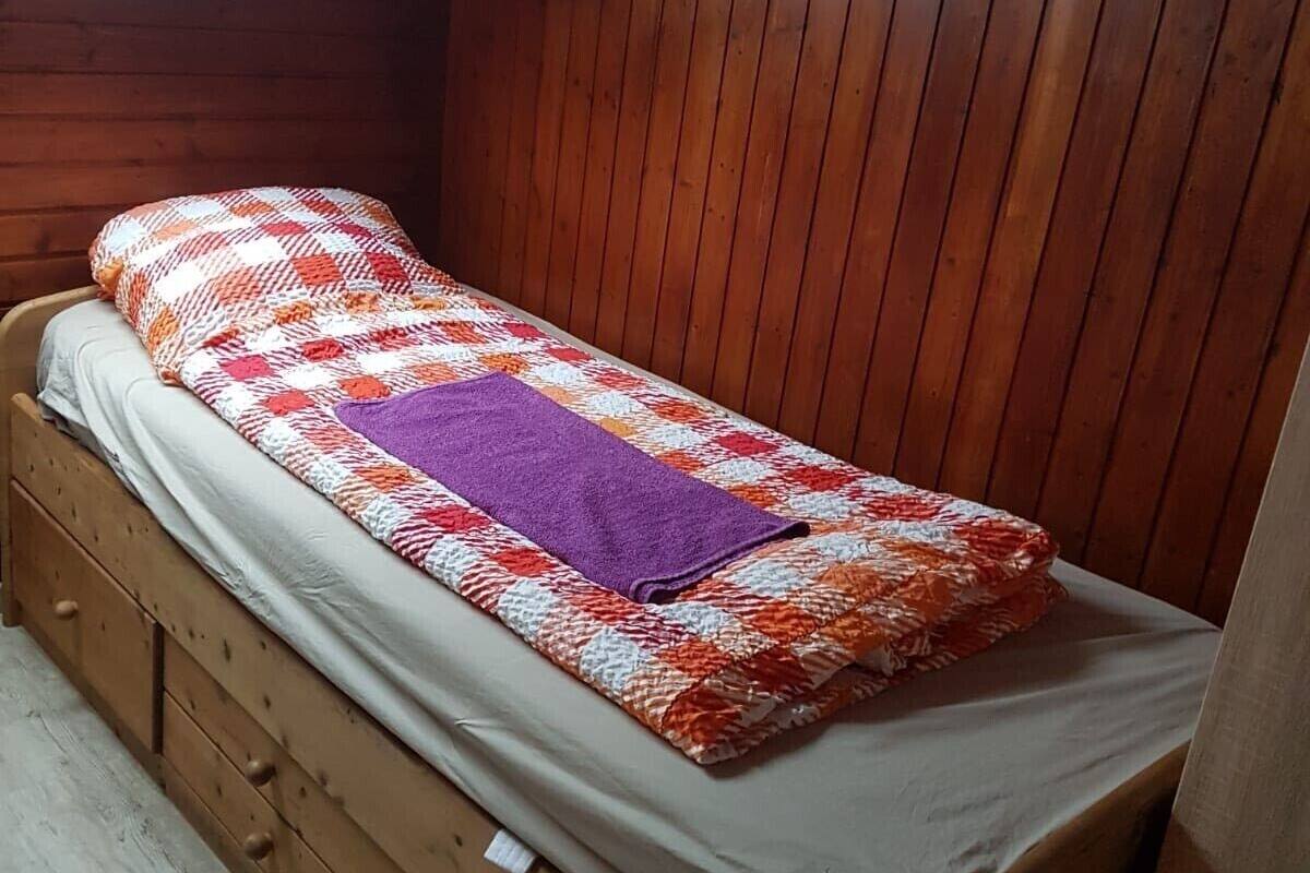 A small, wooden bunk bed with a skylight above, a patterned blanket, and a single pillow.