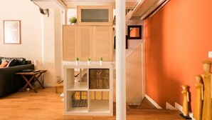 Una sala de estar moderna con piso de madera, un sofá negro, una estantería blanca y una escalera que conduce a un nivel superior.