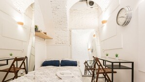 Un dormitorio pequeño con cama, dos sillas, una mesita y un espejo.