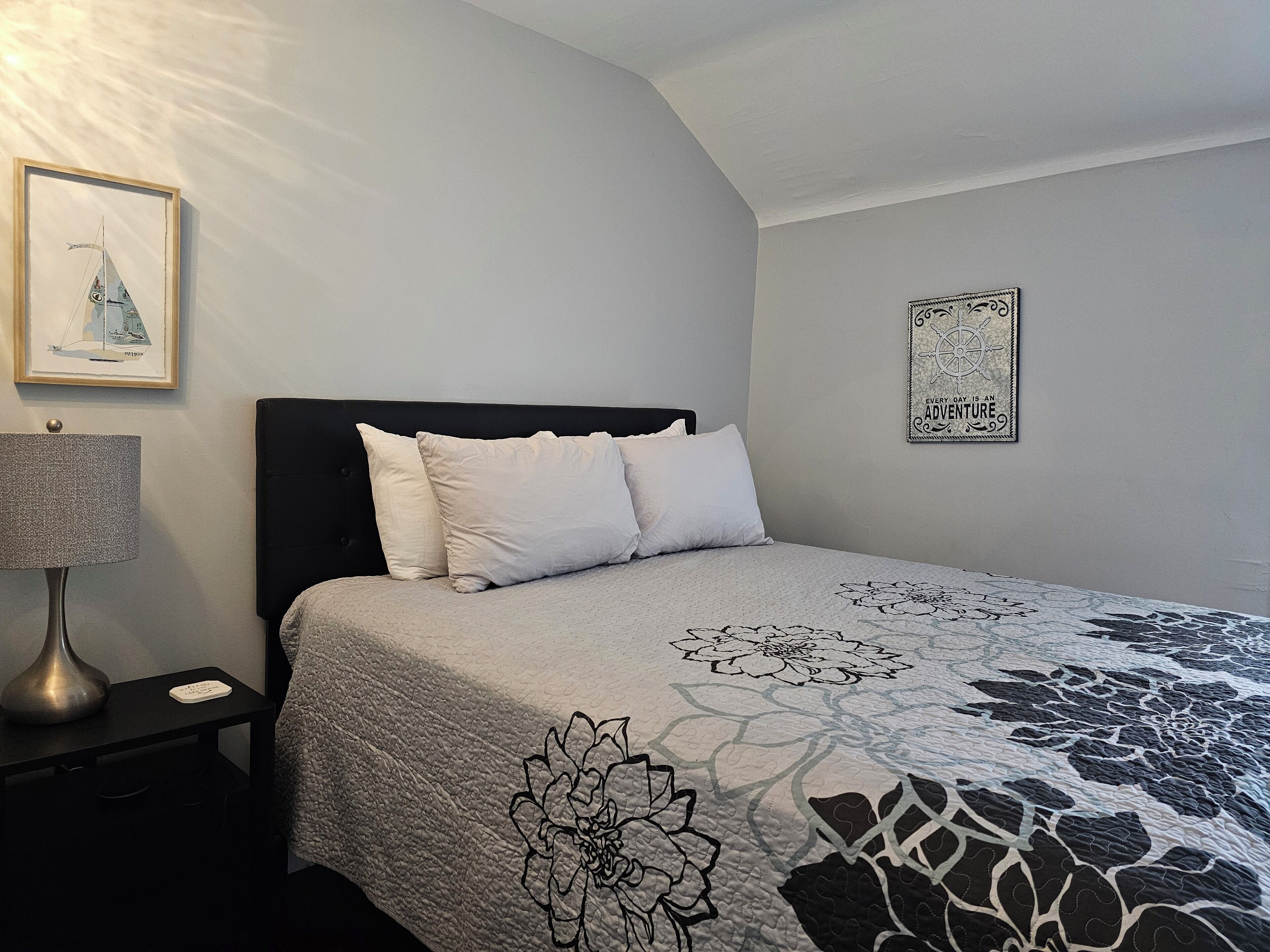 A bedroom with a bed, a nightstand, a lamp, and wall art.