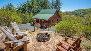 A rustic cabin with a green roof, surrounded by trees and a gravel area with Adirondack chairs. - App State of Mind | Adventure Awaits at Every Turn | Hot Tub & Covered Decks (West Jefferson)