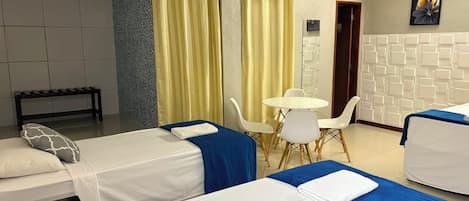 Habitación de hotel con dos camas, una mesita, sillas, un banco y un aire acondicionado instalado en la pared.