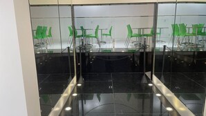 Une salle de conférence dotée d’une cloison en verre, de chaises vertes et d’un sol recouvert de carreaux noirs.