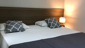 Un lit bien fait, avec une tête de lit sombre, deux oreillers à motifs gris et blancs, et une lampe de chevet.