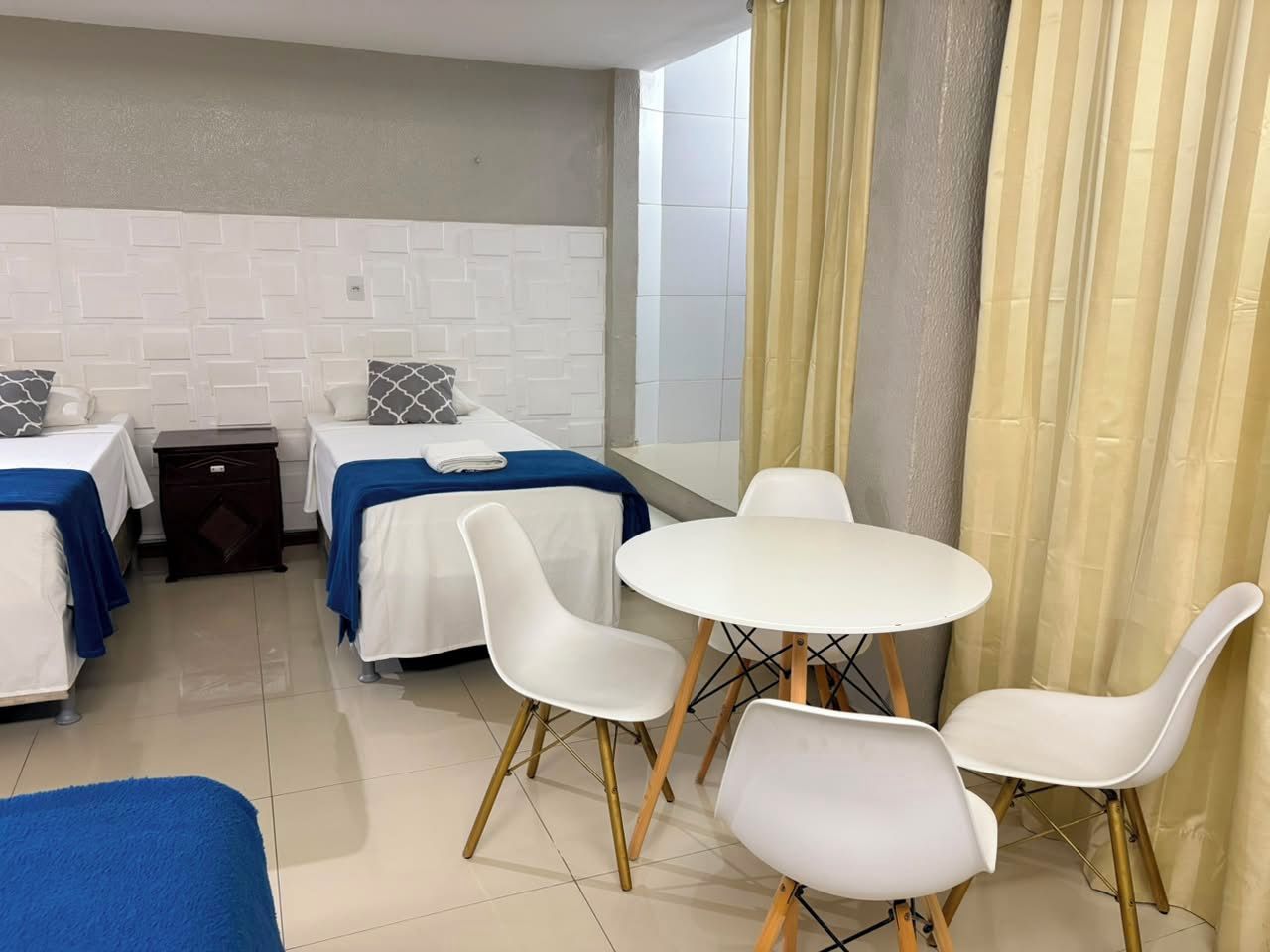 Een hotelkamer met twee bedden, een ronde tafel met stoelen, een kastje en een raam met gordijnen.