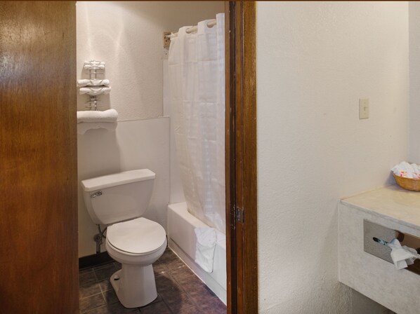 A small bathroom with a toilet, a shower curtain, and a sink with a basket of toiletries.